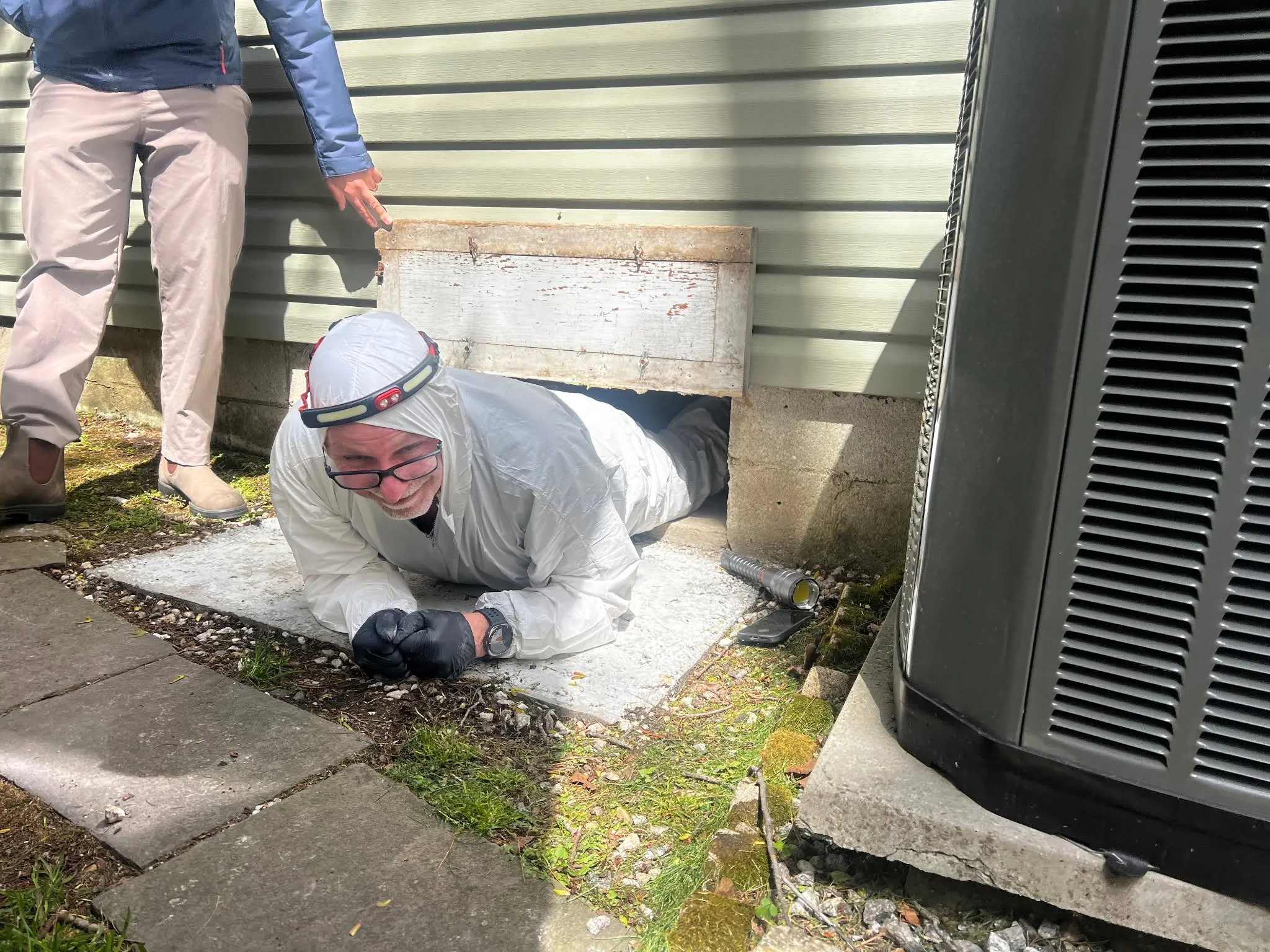 Eagle Eye inspector Lance Kotash in white protective gear and a headlamp at a crawl-space opening